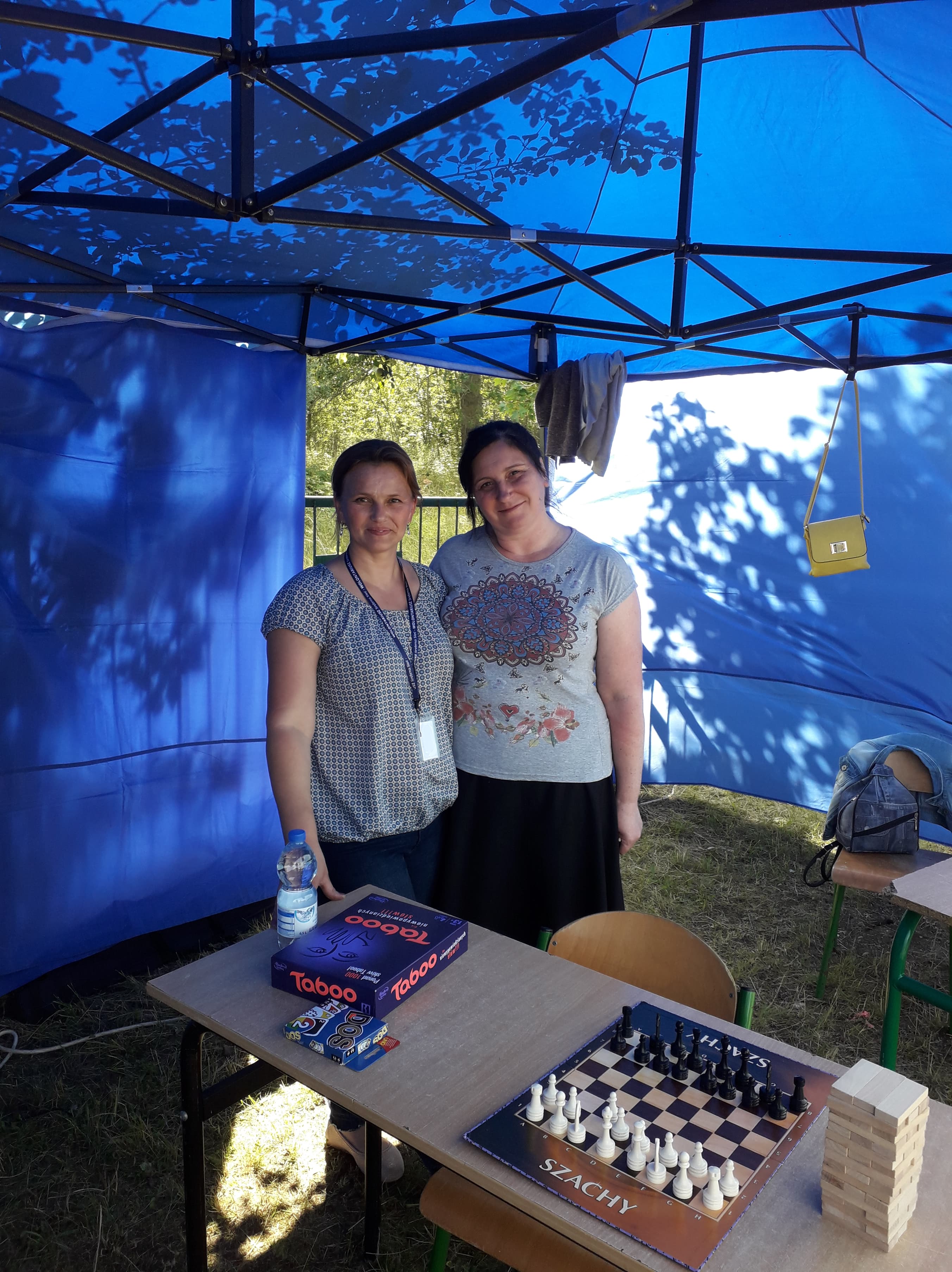 Opiekun wolontariatu senioralnego przy rozstawionych stolikach z grami planszowymi i karcianymi.