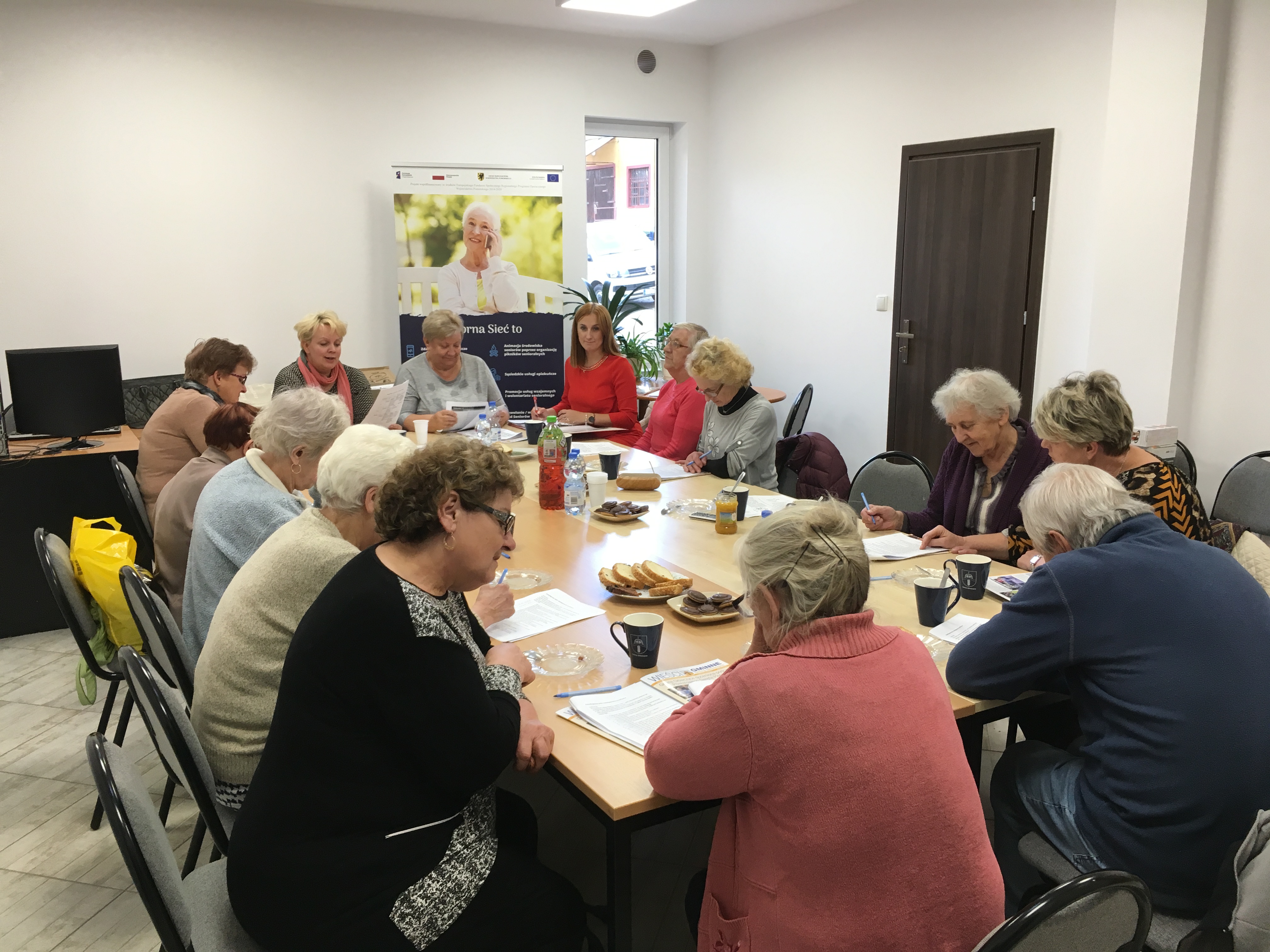 Seniorzy oraz trenerki podczas szkolenia, skupieni wokół stołu.