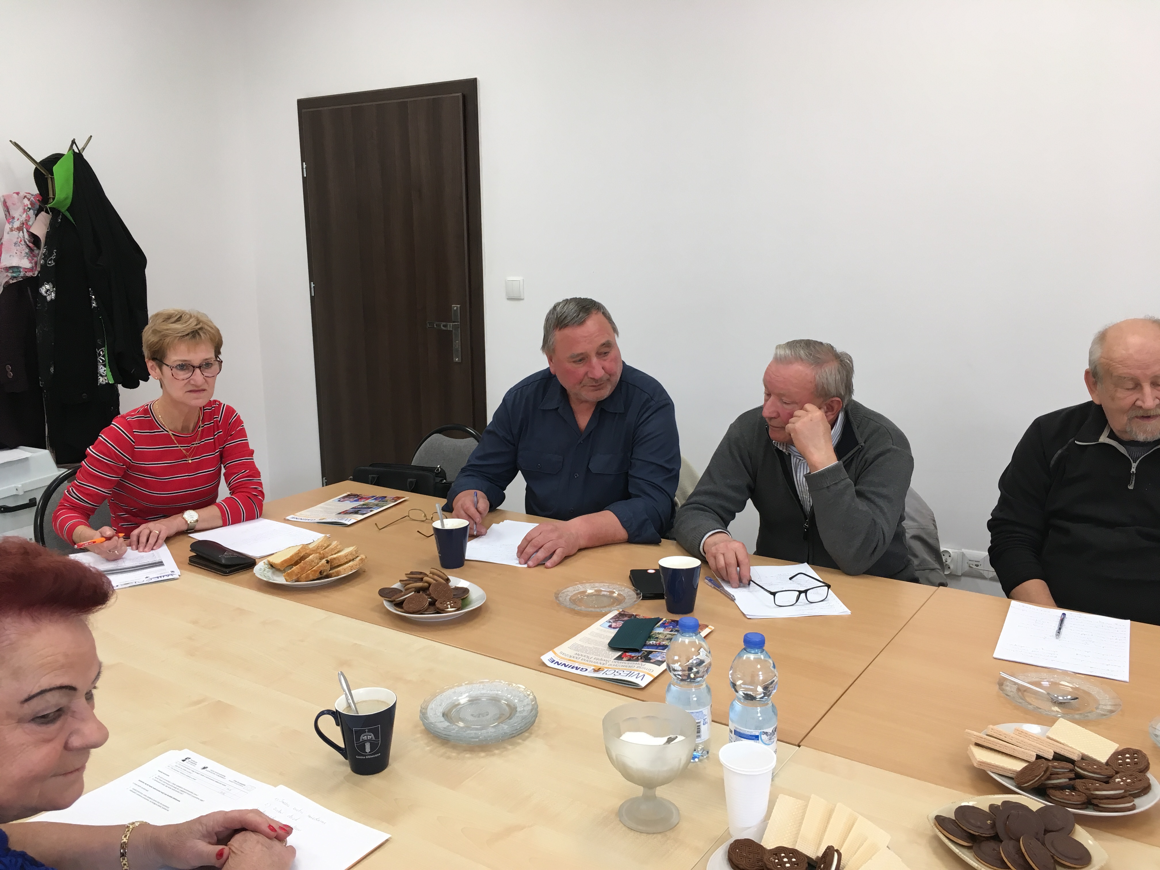 Opiekunowie podczas szkolenia, skupieni wokół stołu, przysłuchujęcy się prowdzącym szkolenie trenerom.