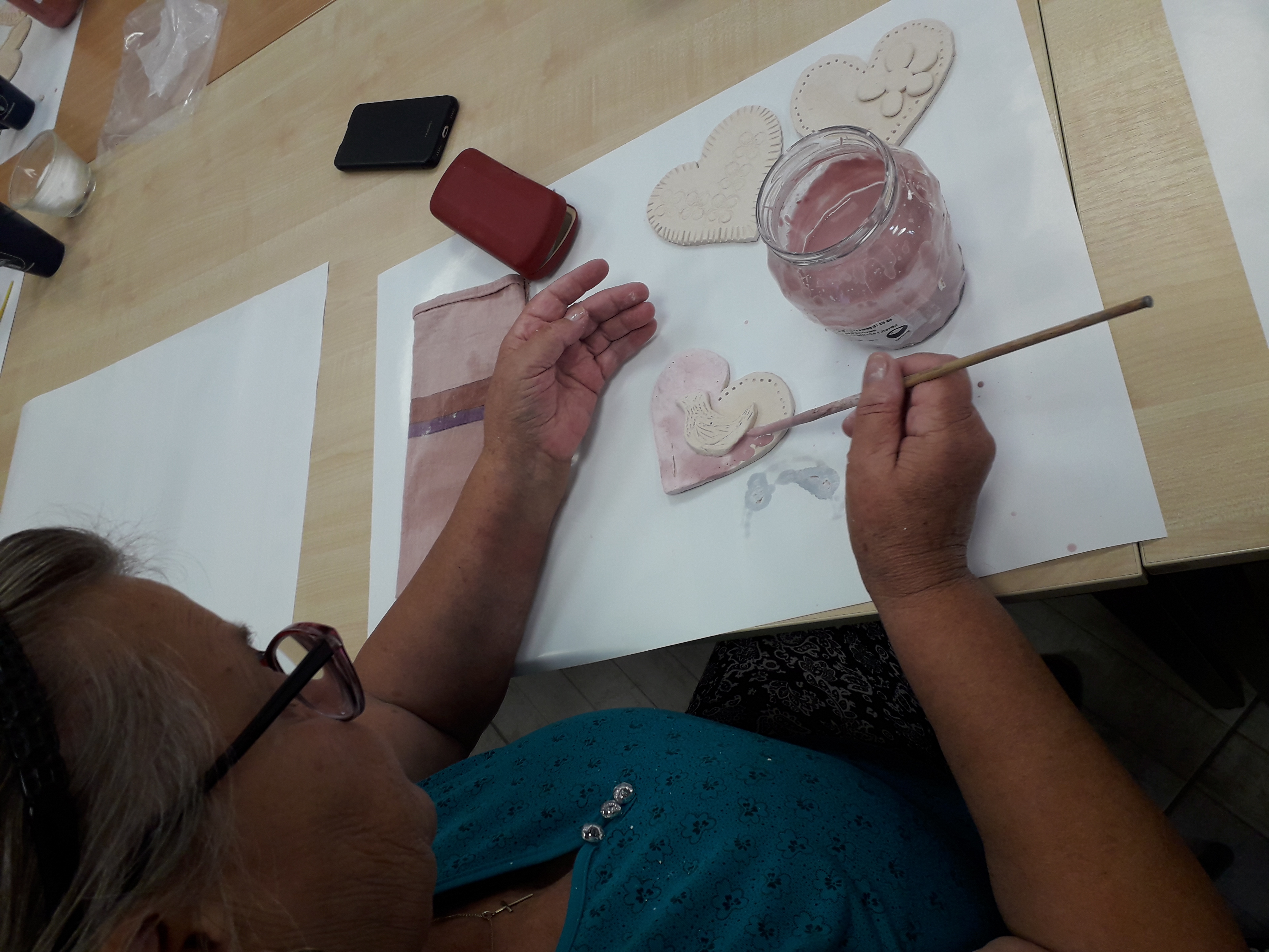 Uczestniczka warsztatów zdobiąca wyschnięte serce z gliny.