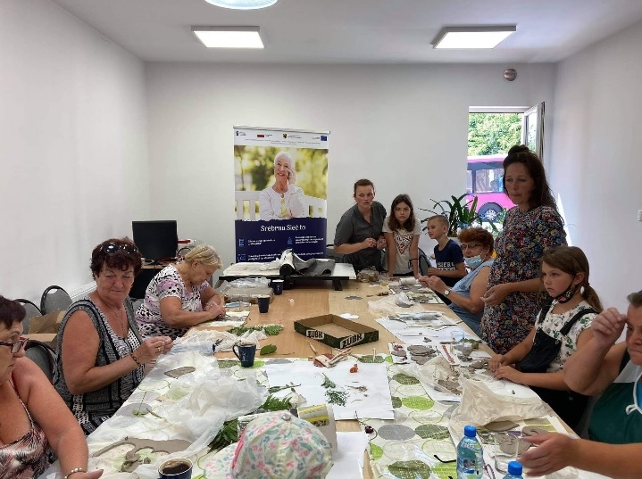 Uczestnicy warsztatów skupieni wokół stołów, tworzący ozdoby z gliny.