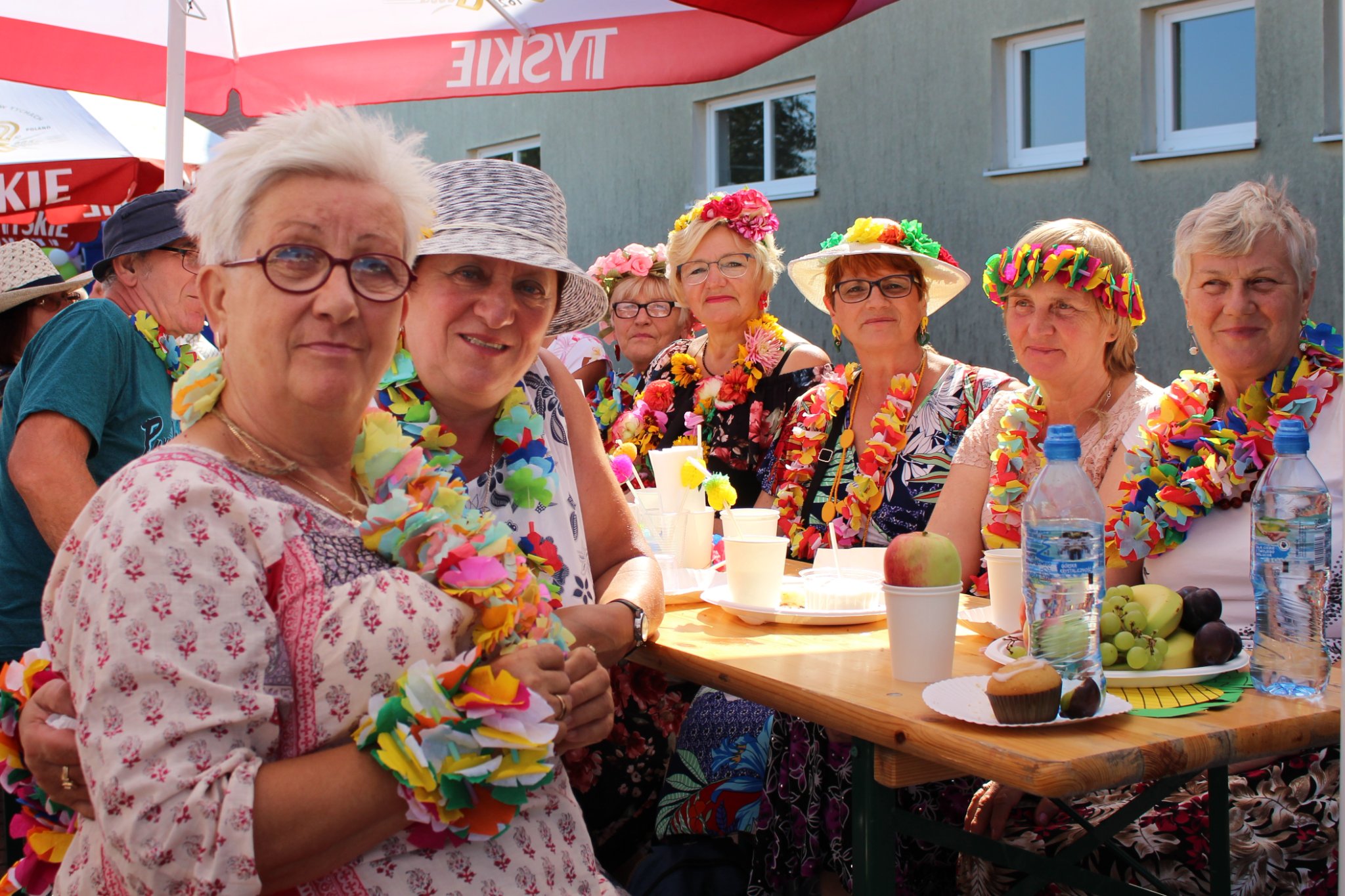 Uczestnicy pikniku zgromadzeni przy stołach pod parasolami