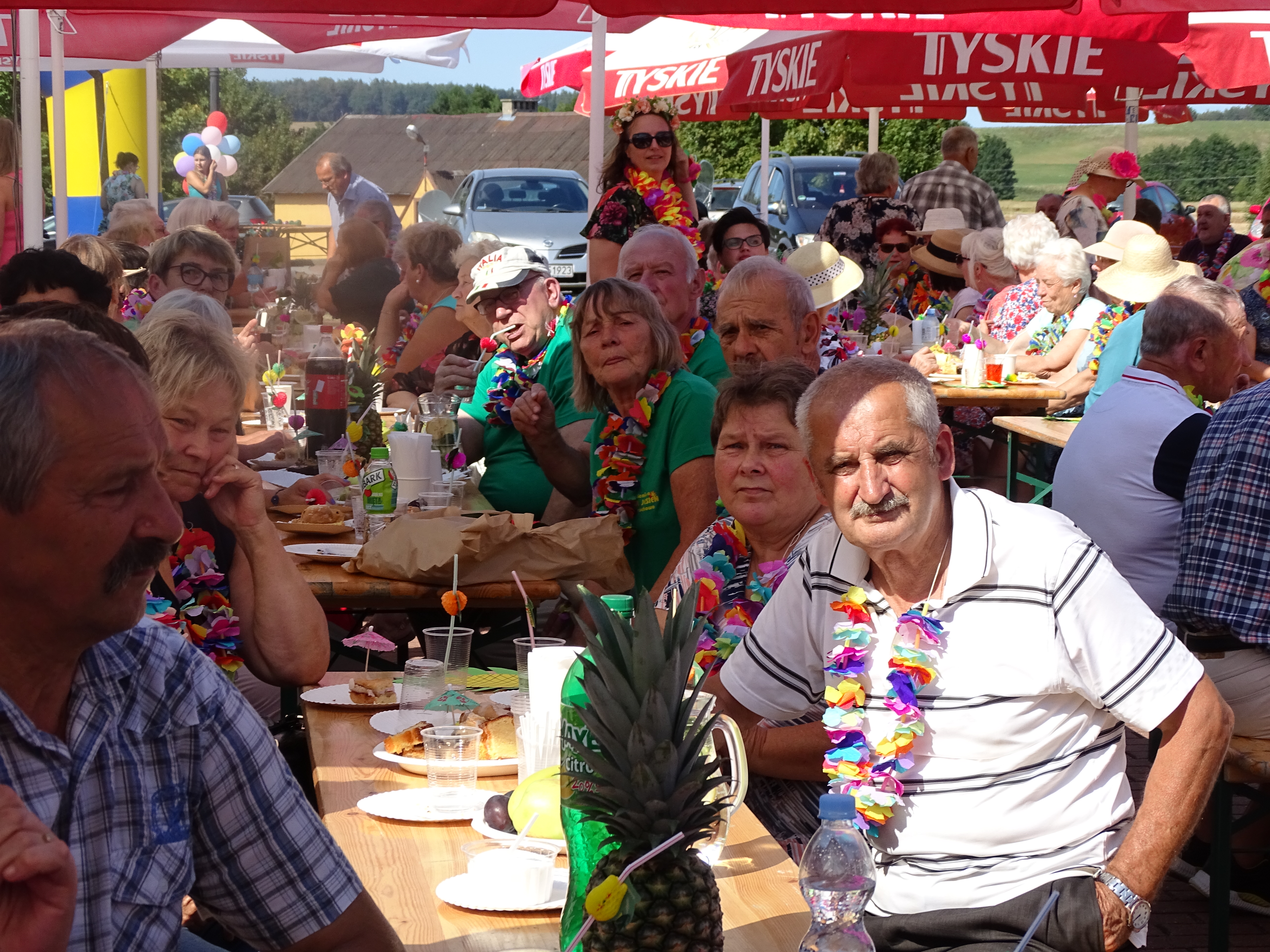 Uczestnicy pikniku zgromadzeni przy stołach pod parasolami