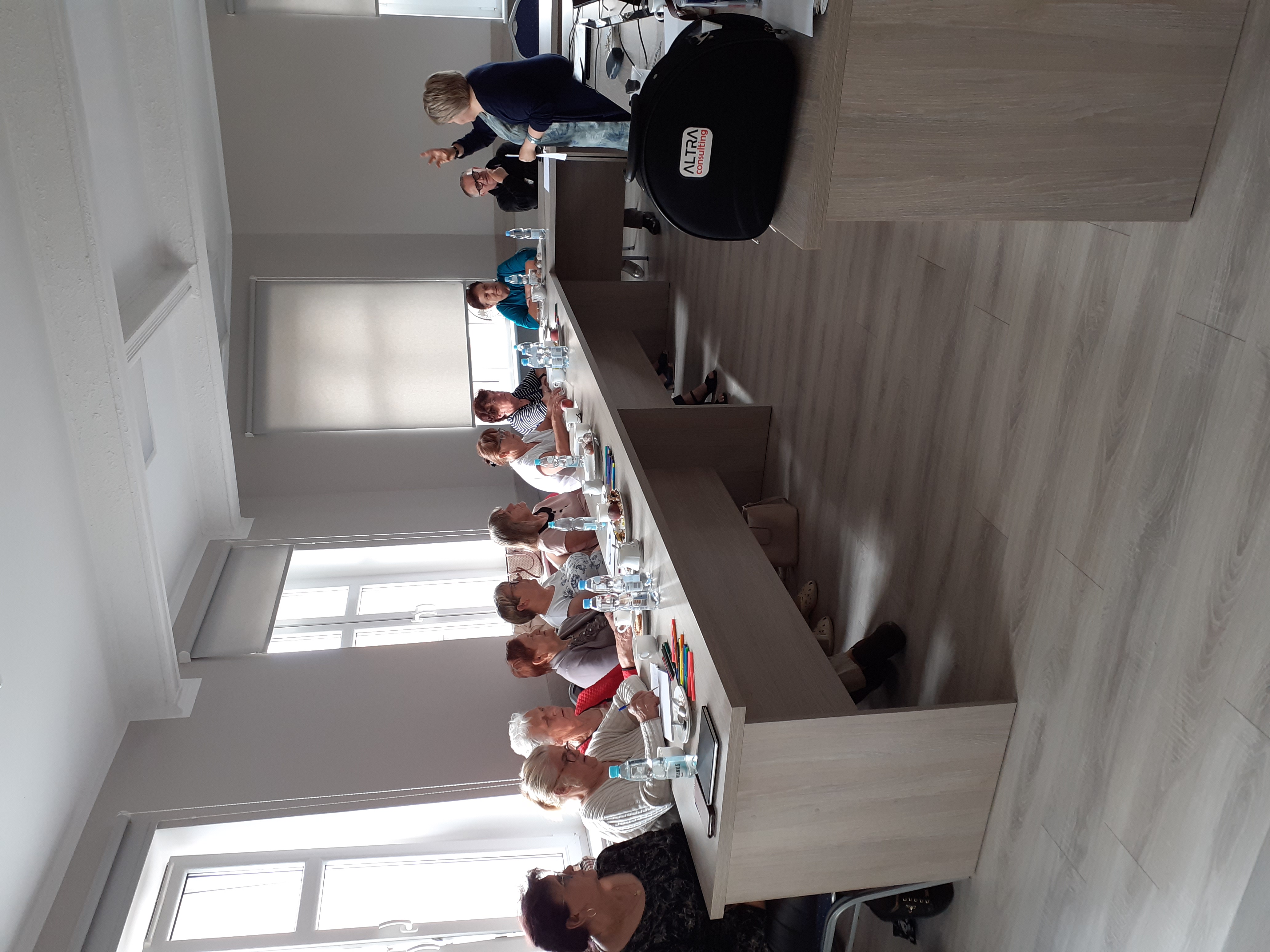 Uczestnicy szkolenia siedzący przy stole i pani szkoląca stojąca przed nimi