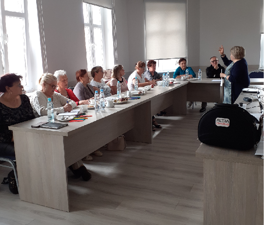 Uczestnicy szkolenia siedzący przy stole i pani szkoląca stojąca przed nimi