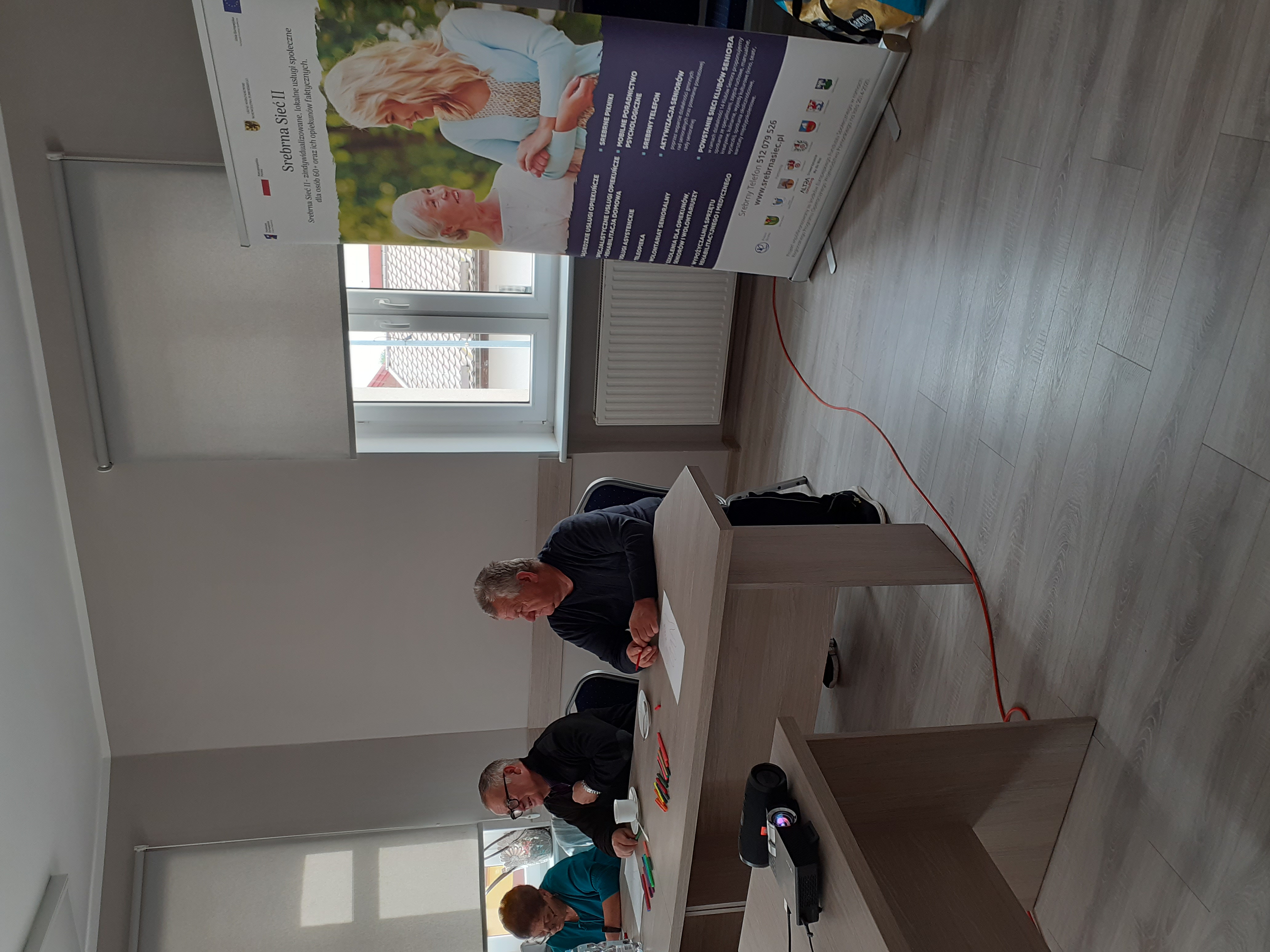 Uczestnicy szkolenia siedzący przy stole, w tle roll-up z plakatem promującym projekt